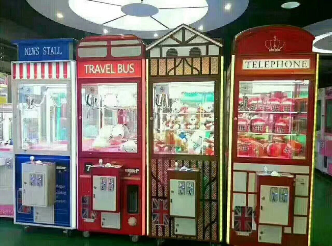 Four themed claw crane machines in an arcade — News Stall, Travel Bus, Tudor House, and Telephone Booth designs — filled with plush toy prizes, LED interior lighting
